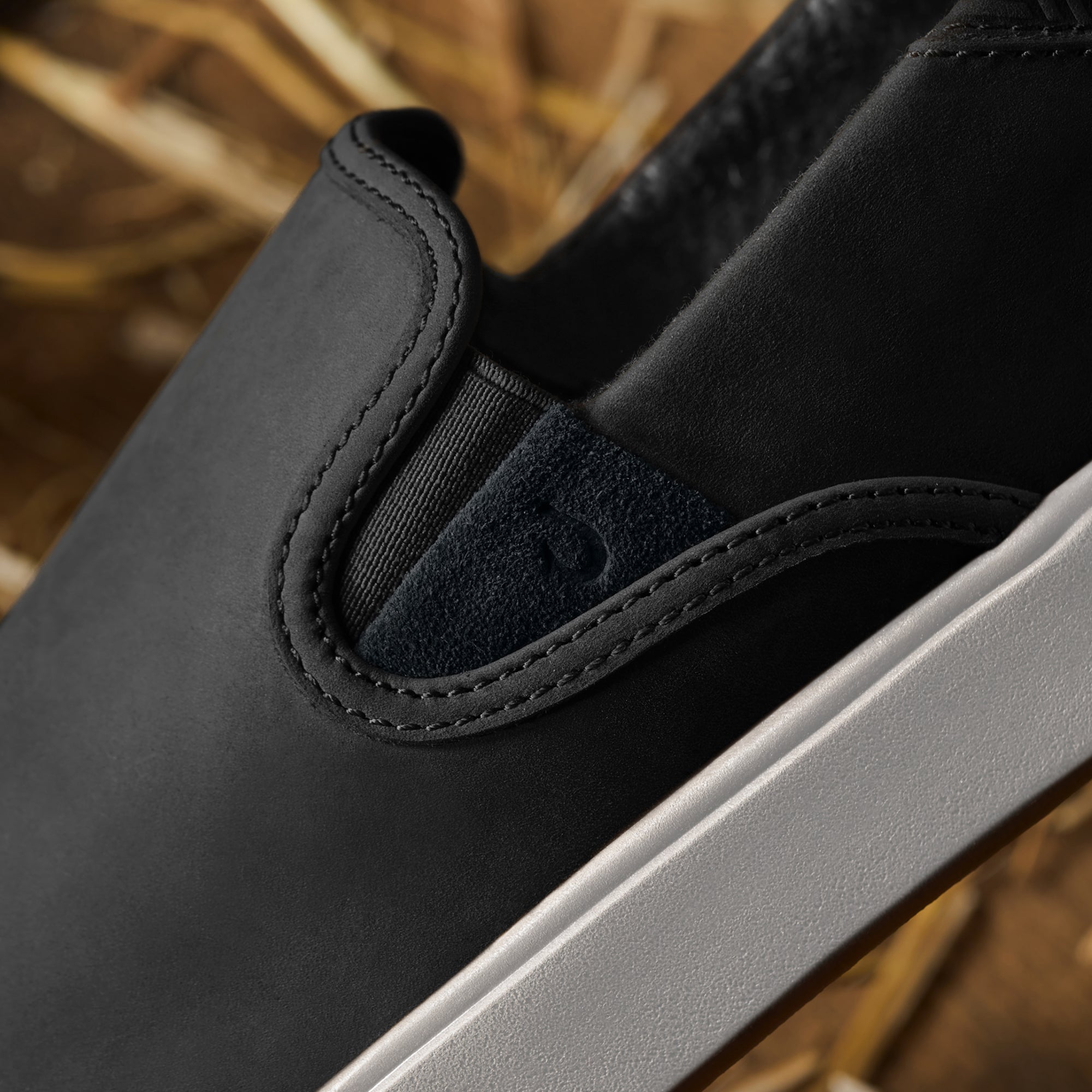 Black slip-on shoe with stitched heel detail and white sole, shown in close-up view.