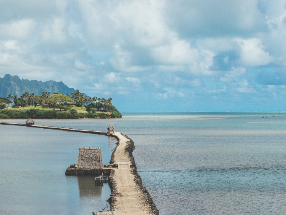 A pier on a beautiful Hawaiian beach with a cloudy blue sky.