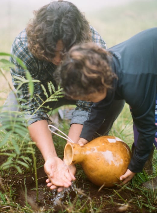 Woman pouring water onto farm soil while a man uses the water to rinse his hands.